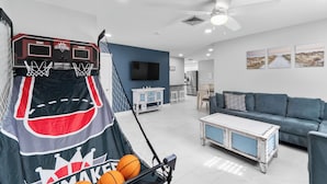 A living room with a basketball hoop, a TV, a sofa, and a coffee table. - Coastal Naples Escape Private Pool, Sleeps 12, Vanderbilt Beach 5 mins away (Naples)