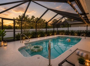 A swimming pool with a glass enclosure, surrounded by plants and a sunset view.