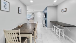 A modern kitchen with a dark wooden countertop, white stools, and a staircase leading to another level. - Coastal Naples Escape Private Pool, Sleeps 12, Vanderbilt Beach 5 mins away (Naples)