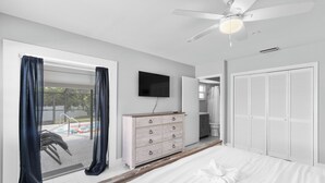 A bedroom with a bed, a dresser, a TV, a ceiling fan, and a view of an outdoor swimming pool. - Coastal Naples Escape Private Pool, Sleeps 12, Vanderbilt Beach 5 mins away (Naples)