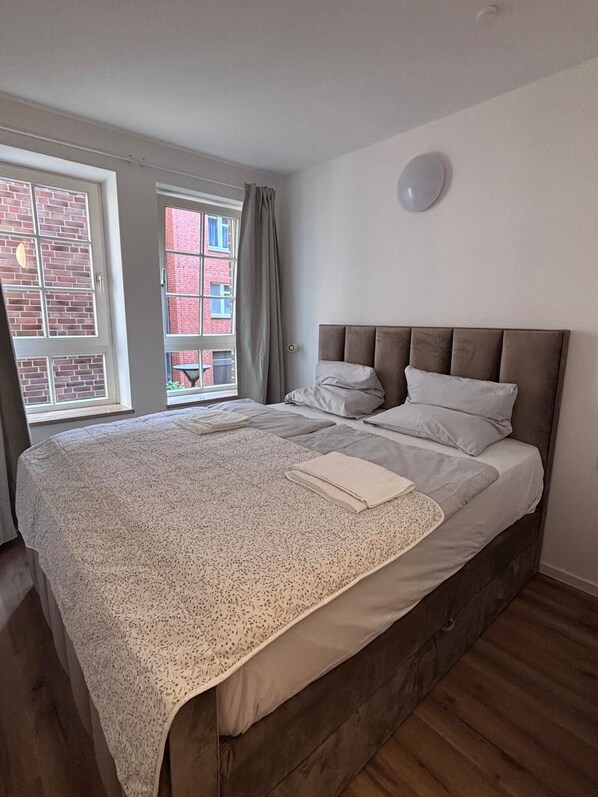 A bedroom with a large bed, a window with curtains, and a view of a brick building. - Vrbo Property (Hamburg)