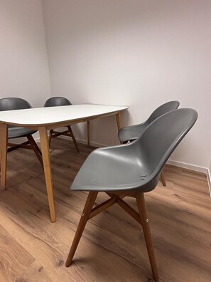 A dining area with a round table and four chairs, wooden flooring, and plain walls. - Vrbo Property (Hamburg)