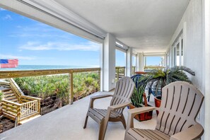 Ein überdachter Balkon mit zwei Adirondack-Stühlen, einer Holzterrasse und Blick aufs Meer.