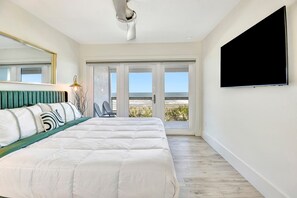 Ein Schlafzimmer mit Bett, Fernseher, Balkon mit Meerblick und einem Sessel.