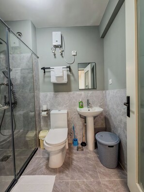 Un baño con cabina de ducha de vidrio, inodoro, lavabo, espejo y cubo de basura.
