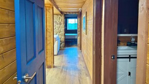 A wooden hallway with a stone wall, a bed, and a window with a view. - Luxury Renovated | Pool | Hot Tub | Sleeps 20 (New Plymouth)