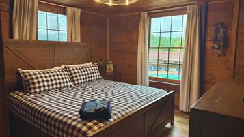 A wooden cabin room with a bed, a desk, and a window overlooking a pool.