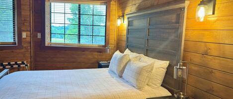 A wooden cabin bedroom with a bed, bedside table, and a window.