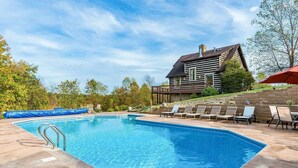 A rectangular swimming pool with a metal ladder, surrounded by lounge chairs and a wooden deck.