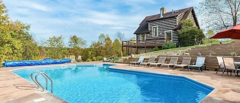 Piscina rectangular con escalera metálica, rodeada de sillones de descanso y una terraza de madera.