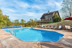 Piscina rectangular con escalera metálica, rodeada de sillones de descanso y una terraza de madera.