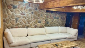 A room with a stone wall, a beige sofa, a wooden coffee table, and a patterned rug.