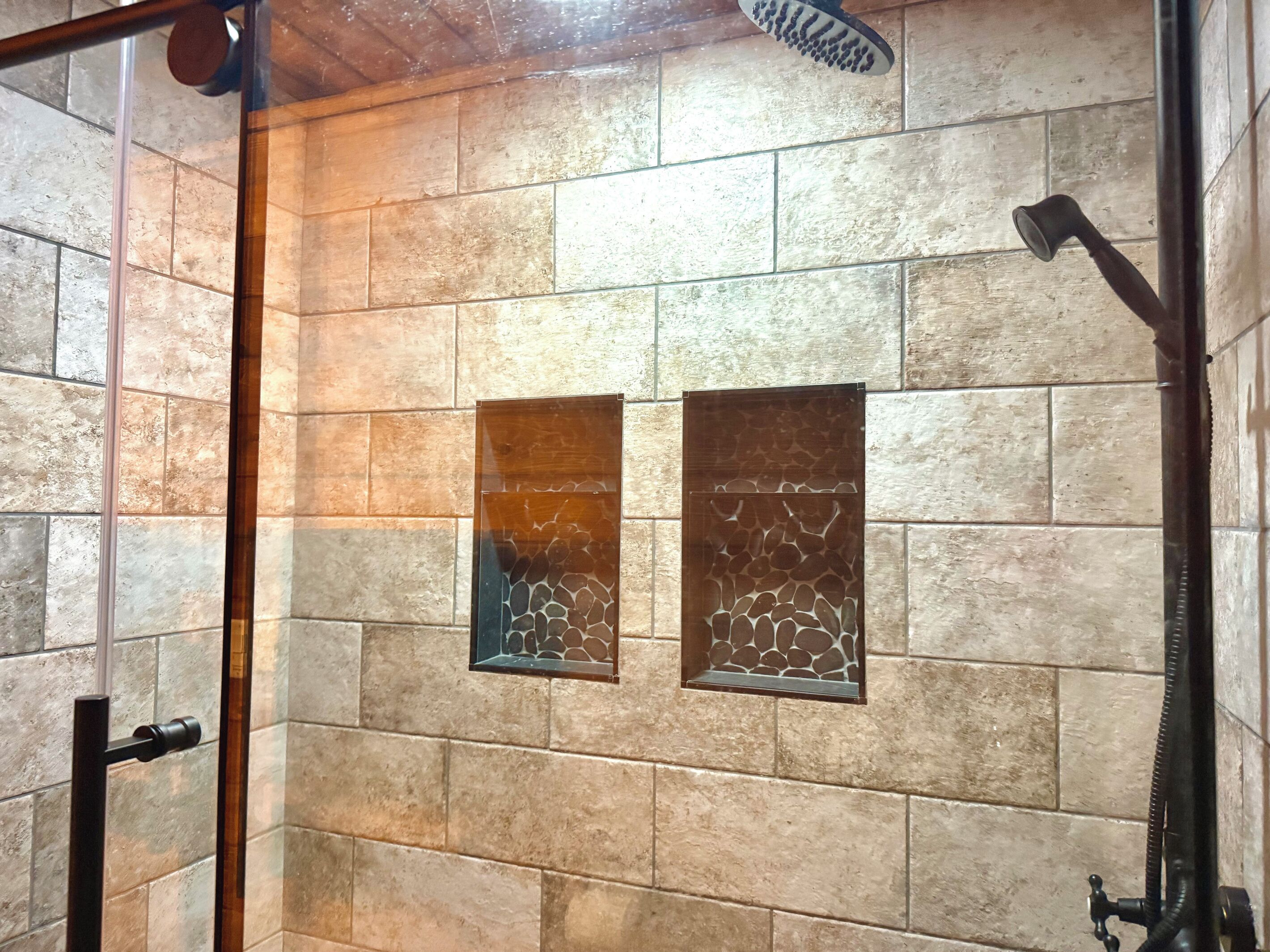 A shower with a glass door, a handheld showerhead, and a wall-mounted faucet.