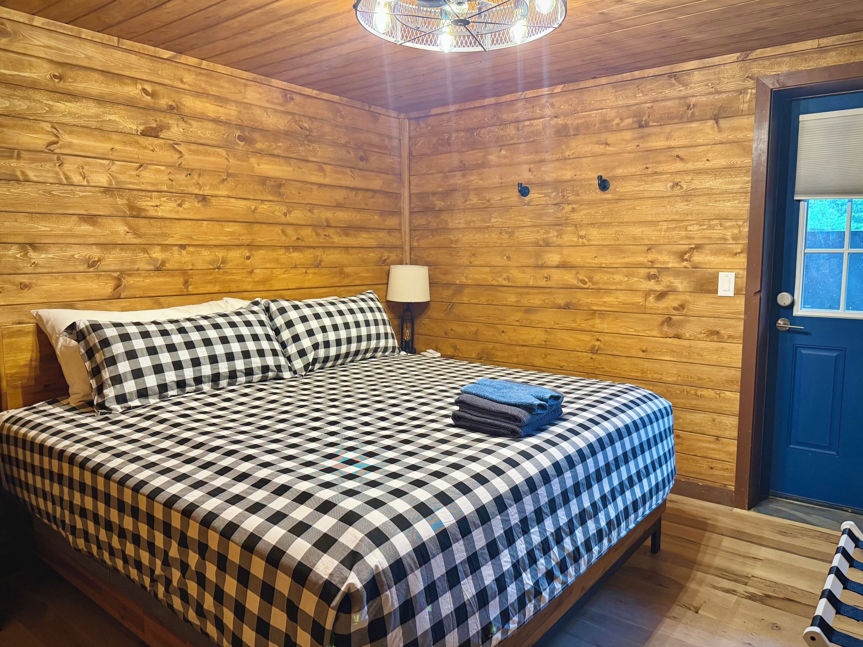 A wooden-paneled room with a bed, a lamp, and a door.