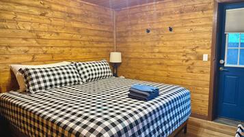 A wooden-paneled room with a bed, a lamp, and a door.