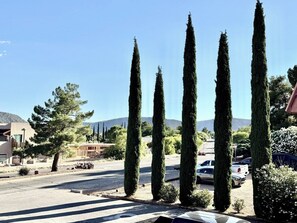 Um estacionamento com altas árvores cipreste, um edifício com telhado inclinado e uma montanha ao fundo.