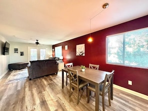 Una sala de estar moderna con comedor, piso de madera, un sofá, una mesa de comedor con sillas y una cocina al fondo.