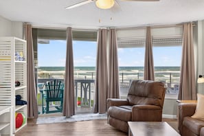 A room with a view of the ocean, a ceiling fan, a leather chair, and a wooden table. - Oceanfront Condo, Patio, Pool & Beach Access (Ormond Beach)