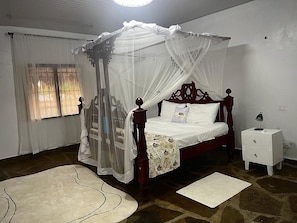 Ein Schlafzimmer mit Himmelbett, Nachttisch und einem Fenster mit Vorhängen.