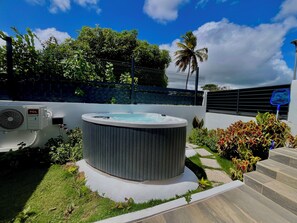 A hot tub surrounded by greenery, a fence, and a palm tree. - Vrbo Property (Les Abymes)