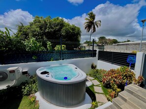 A hot tub surrounded by greenery, a fence, and a clear sky. - Vrbo Property (Les Abymes)