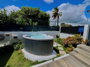 A hot tub surrounded by a garden with a palm tree and a fence. - Vrbo Property (Les Abymes)
