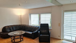 A living room with a black leather sofa, a glass coffee table, a black leather armchair, and a floor lamp.