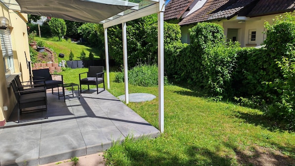 Eine überdachte Terrasse mit Gartenmöbeln, ein Garten und ein Haus im Hintergrund.