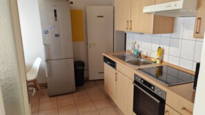 Eine kleine Küche mit Kühlschrank, Geschirrspüler, Backofen und Spüle mit Holz Arbeitsplatte.