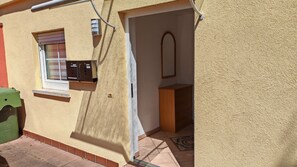 L’extérieur d’un bâtiment avec une boîte aux lettres, une fenêtre avec des stores, une porte et un petit meuble.