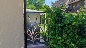 Un jardin avec un portail en métal, un chemin et une maison avec un toit en tuiles en arrière-plan.