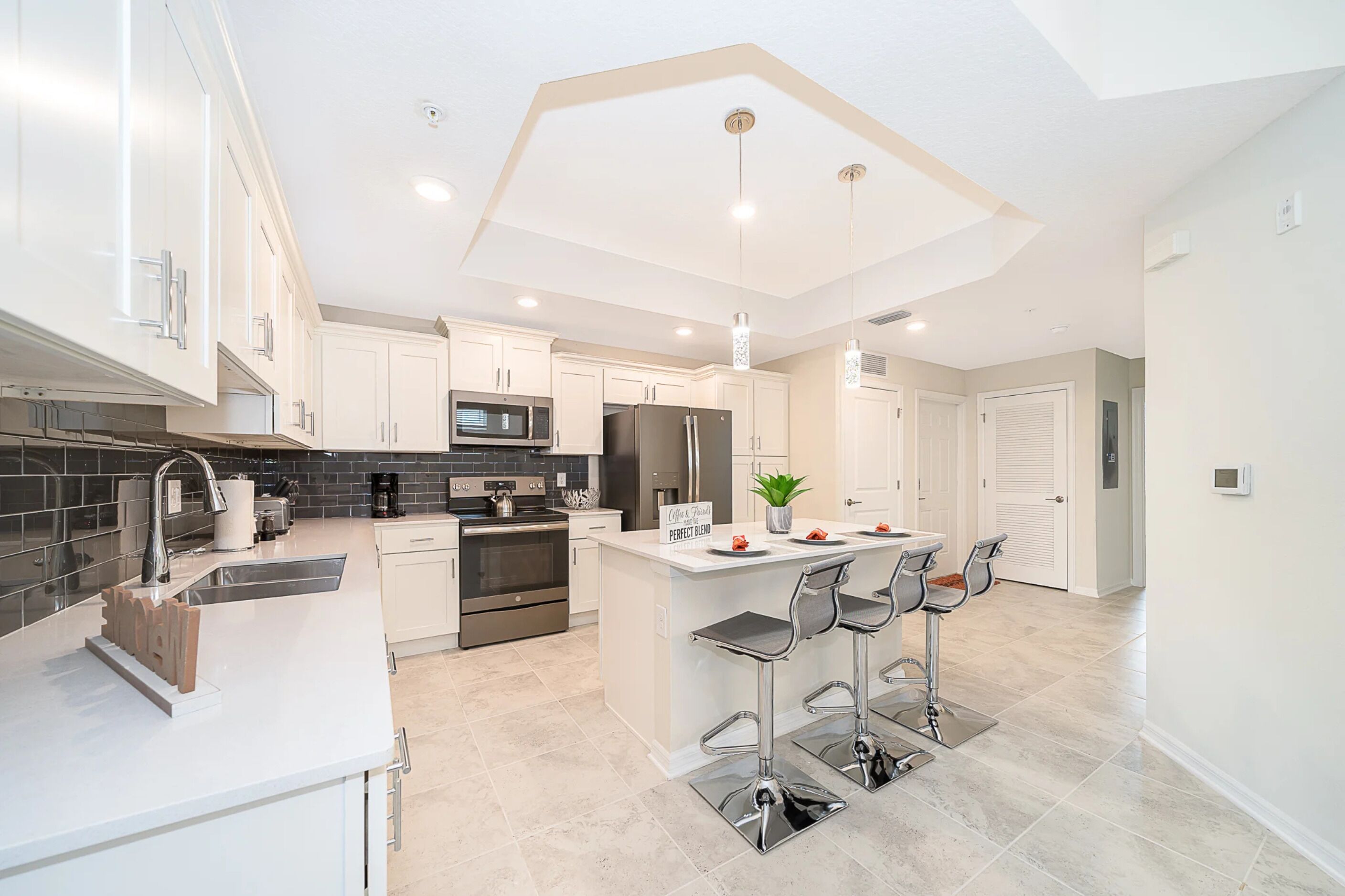 A modern kitchen with white cabinets, stainless steel appliances, and a central island with bar stools.