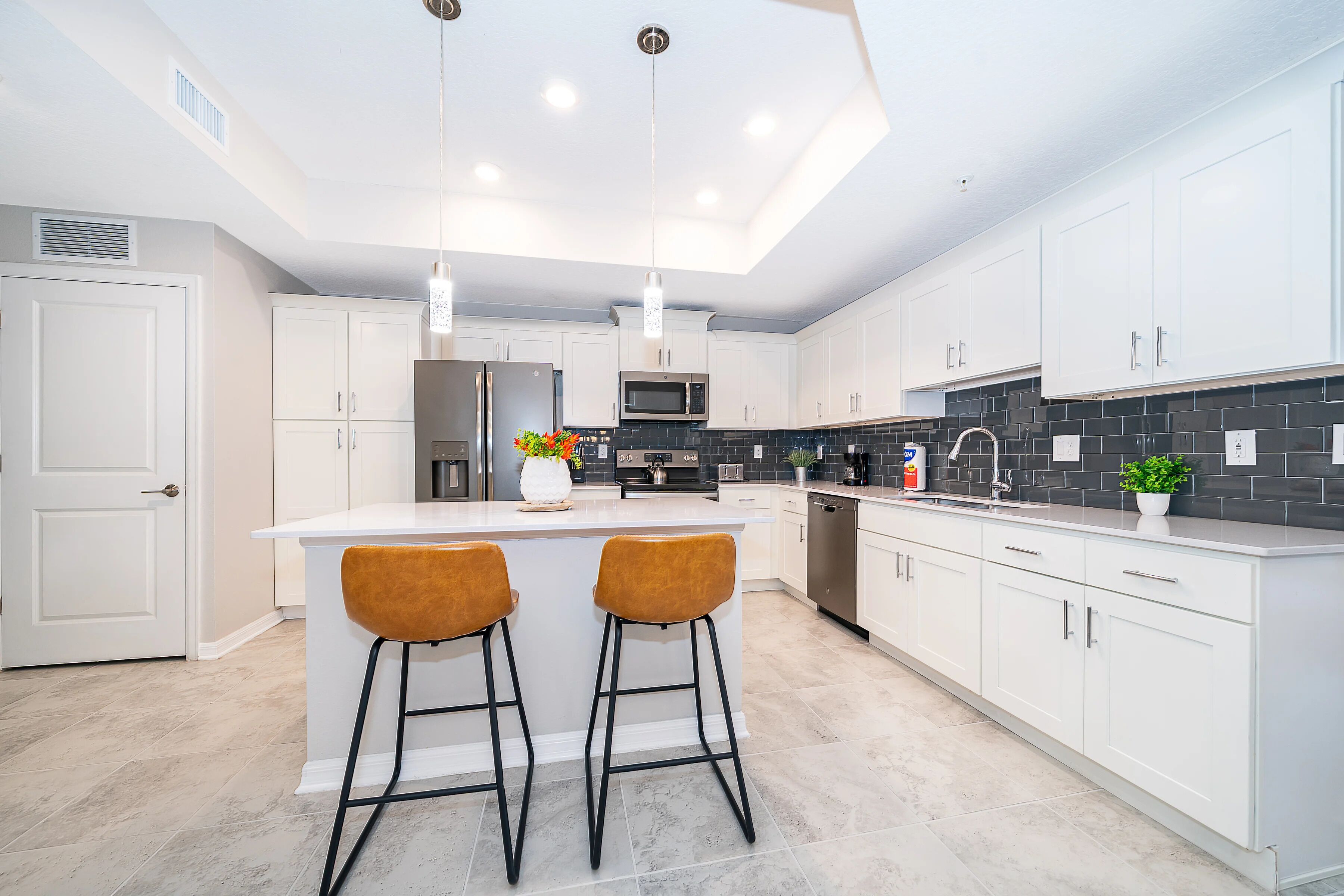 A modern kitchen with white cabinets, a central island with stools, a microwave, and a stainless steel refrigerator.