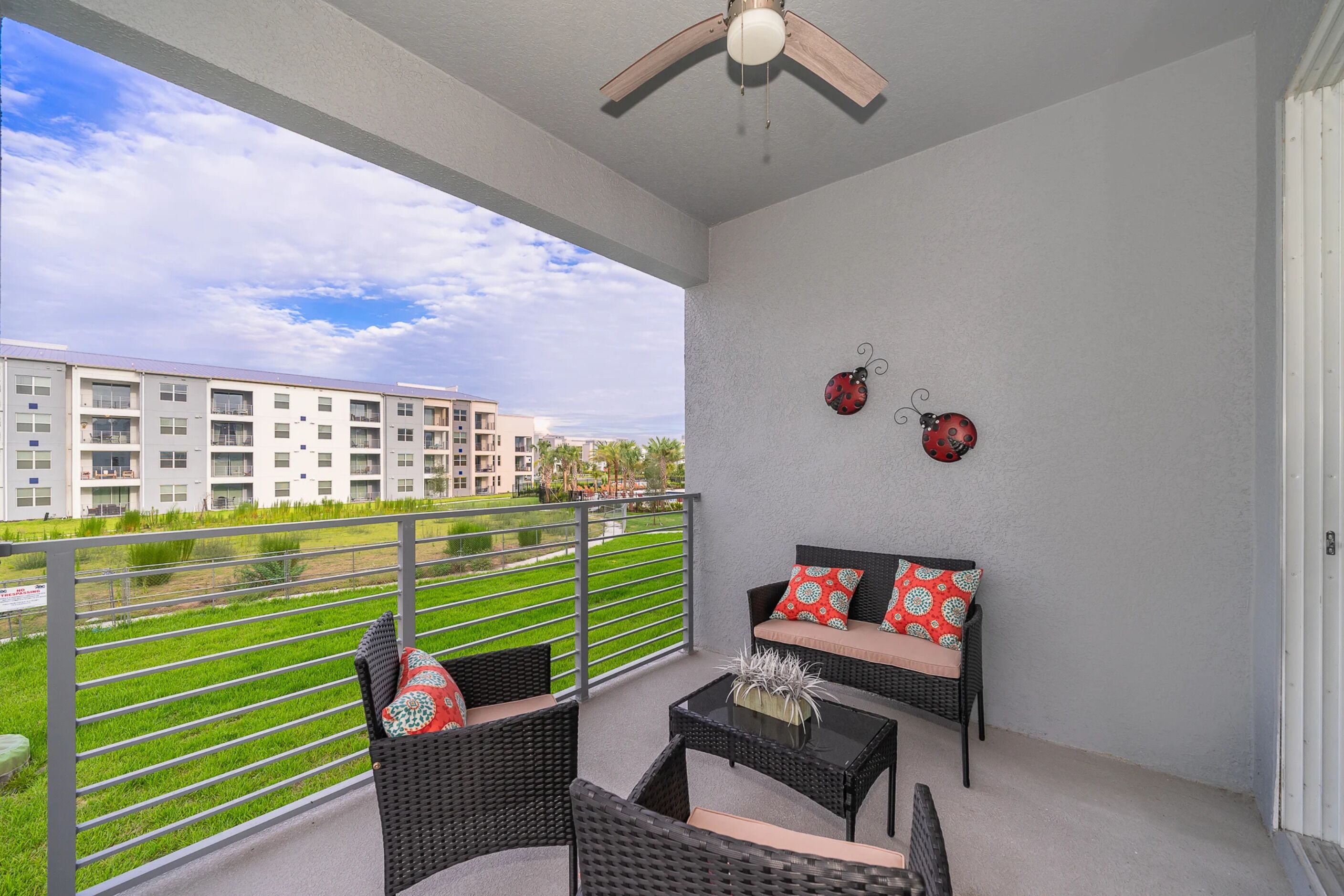 A balcony with wicker furniture, a ceiling fan, and decorative ladybug wall art.