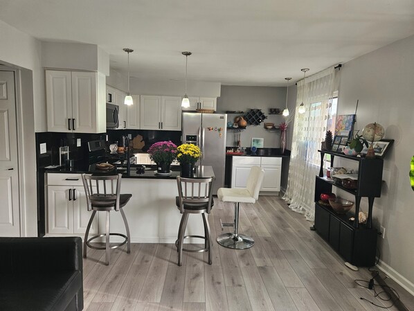 A modern kitchen with white cabinetry, a central island with bar stools, and a dining area.
