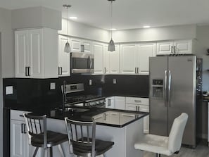 A modern kitchen with white cabinetry, a black countertop island, stainless steel appliances, and pendant lighting.
