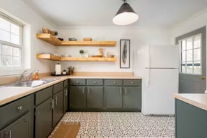 A kitchen with dark cabinets, wooden shelves, a patterned floor, and a pendant light.