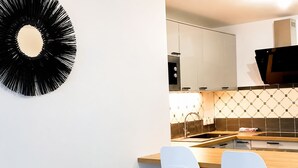 A modern kitchen with white cabinets, a black circular wall decoration, and two white chairs. - Melody Clamart, 25 min from Paris, Tramway 6, Parking (Clamart)