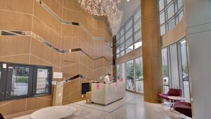 Un vestíbulo amplio con mostrador de recepción, una escalera y grandes ventanales que ofrecen vistas al exterior.