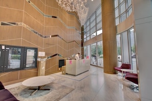Eine geräumige Lobby mit einer Rezeption, einer Treppe und großen Fenstern, die einen Ausblick nach draußen bieten.