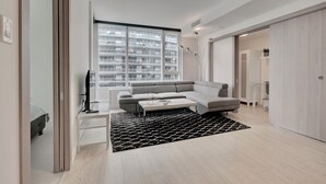 Una sala de estar moderna con un sofá gris, una mesa de centro, un tapete blanco y negro y un ventanal con vistas a la ciudad.