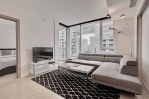 Een moderne woonkamer met een flatscreen televisie, een bank, een salontafel en een groot raam met uitzicht op de stad.