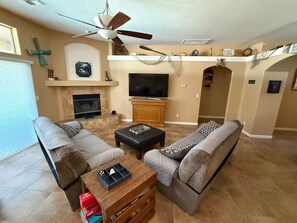 A living room with a fireplace, a ceiling fan, and a television.
