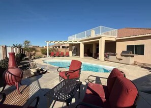Un espace piscine avec des chaises rouges, une table et un barbecue.