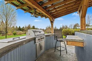 Une cuisine extérieure équipée d’un barbecue, d’un évier et d’une chaise.