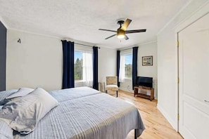 Une chambre à coucher comprenant un lit, un ventilateur de plafond, une chaise, un bureau et une fenêtre avec des rideaux.