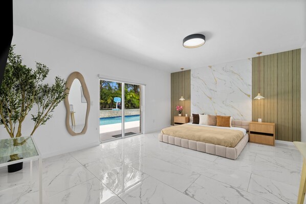 Un dormitorio moderno con una cama grande, un ventanal de vidrio que da a una piscina y vistas de vegetación.