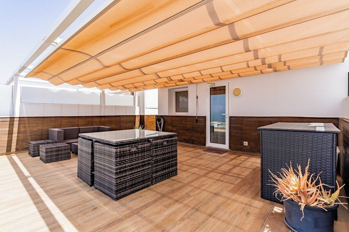 Een terras met een houten vloer, een grote parasol en een tafel van zwart riet.