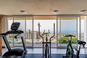 A gym with a treadmill, elliptical, and stationary bike, large windows with a city view. - Premium Penthouse · Private Terrace · Ocean View (Adeje)
