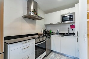 A modern kitchen with white cabinets, a black countertop, stainless steel appliances, and a patterned rug. - Premium Penthouse · Private Terrace · Ocean View (Adeje)